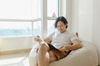 © Sevendeman - Asian man relax and reading book on bean bag sofa in his apartment.