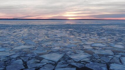 Wall Mural - Broken thick ice pieces floating on calm water surface near river bank at bright purple sunset on cloudy sky in winter aerial view