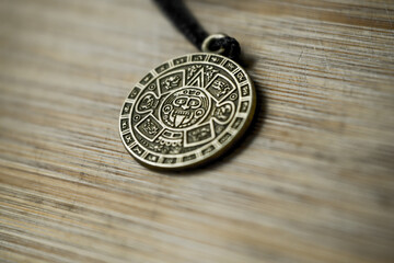 Aztec calendar amulet on a wooden background close-up.