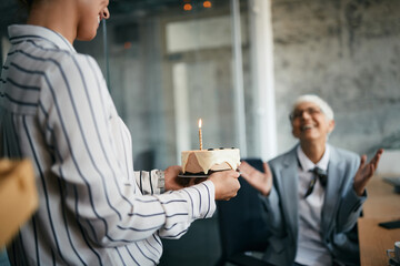 Wall Mural - Close-up of businesswoman carries Birthday cake while surprising her female executive in the office.