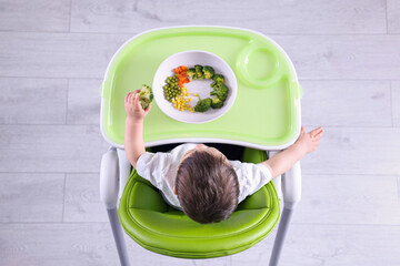 Poster - Cute little baby eating healthy food in high chair indoors, top view