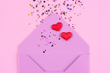 Valentine's Day Festive Background. Closeup View Of Purple Envelope With Red Hearts And Confetti Around On Trendy Pink Background With Copy Space. Flat Lay, Top View