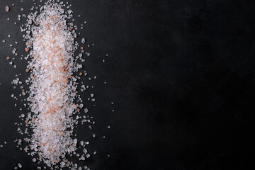 Pink himalayan salt scattered and isolated on a black background, top view, flat lay, copy space