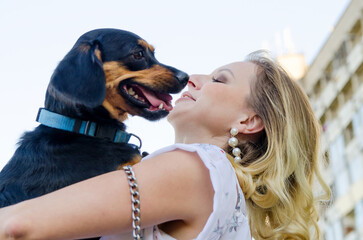 Wall Mural - A cute dog licks a beautiful blonde young woman in a light dress