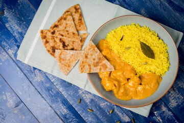 Wall Mural - A top view of cooked Indian food chicken korma with pilau rice and cardamom seeds on a wooden table