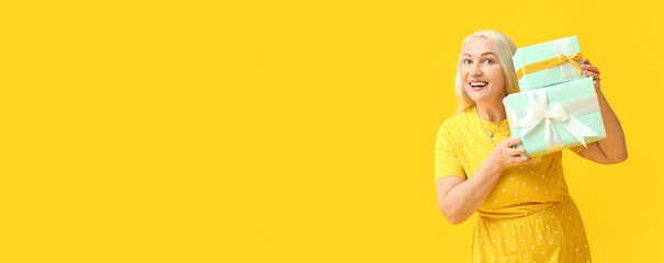 Wall Mural - Smiling mature woman with gifts on yellow background with space for text. International Women's Day celebration