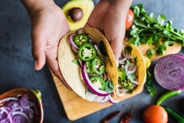 latin woman hands preparing mexican tacos with pork carnitas, avocado, onion, cilantro, and red sauce in Mexico