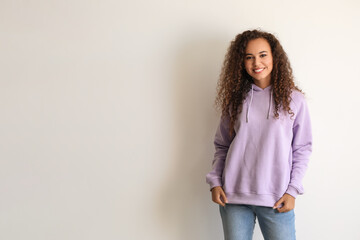 Wall Mural - Beautiful young African-American woman in stylish hoodie on light background