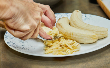 Wall Mural - Chef grinds banana with fork for making pie in the home kitchen