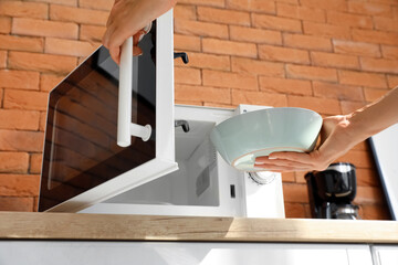 Woman taking bowl with delicious food from microwave oven on wooden counter