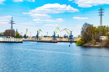 Mounting cranes on the river bank extract sand. Extraction of sand from the bottom of the river. Ships and barges on the water. High voltage electric power line. Ecology. Industrial landscape.