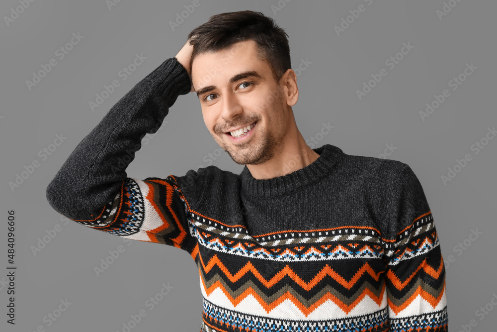 Handsome young man in knitted sweater on grey background