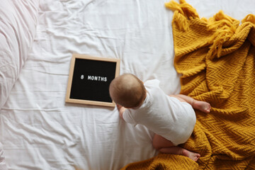 Canvas Print - Caucasian blonde baby eight months old lying on cozy bed with yellow knitted blanket at home. Kid wearing white clothing 