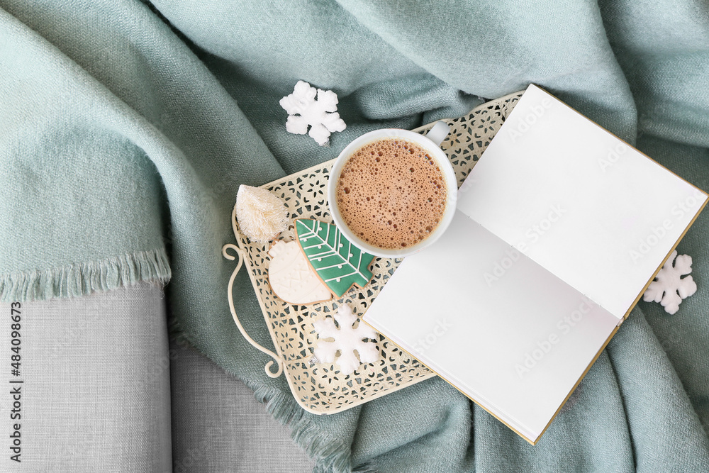 Tray with cup of coffee, winter decor and opened book on sofa