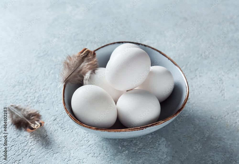 Bowl with white Easter eggs and feathers on grunge background