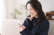 © lielos - ソファーに座りスマートフォンを見ている日本人女性、自宅リビング