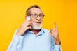 © Tatiana - old man in a blue shirt and glasses talking on the phone yellow background