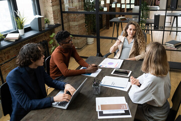 Poster - Confident pregnant female manager speaking to one of colleagues at working meeting by large table in office