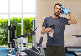 Poster - fitness, sport and healthy lifestyle concept - tired man in sports clothes with protein shake bottle wiping his forehead with towel over gym background