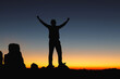 © AungMyo - Successful people silhouette with open arms on rock morning sunset sky background.