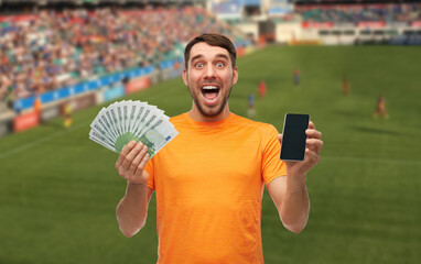 Wall Mural - online betting, gambling and people concept - happy laughing man with smartphone and money over soccer stadium background