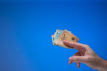 Euro Currency Banknotes Held By Male Hand. Close Up Studio Shot, Isolated On Blue Background