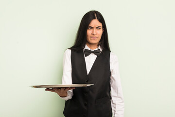 Wall Mural - young pretty hispanic woman feeling sad, upset or angry and looking to the side. waiter with tray concept