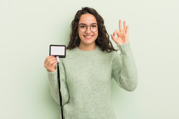 Wall Mural - young pretty hispanic woman feeling happy, showing approval with okay gesture. accreditation card id