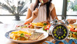 Selective focus of  Alarm clock with woman eating a healthy food as Intermittent fasting, time-restricted eating-Diet breakfast concept