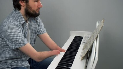 Wall Mural - Disabled brunet young man with amputated two stump hands is playing piano by notes looking at camera. Life of handicapped person musician with disabilities. He's trying to keep playing after injury.