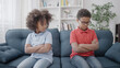 Offended black sister looking at angry brother sitting on sofa, conflict between siblings