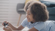 © Synthex - Happy african american girl enjoying video gaming experience, lying on floor
