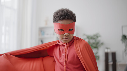 Wall Mural - African american little boy wearing superhero costume, playing game at home