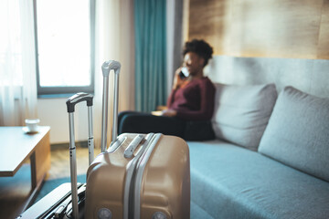 Wall Mural - Close-up of luggage and blurred background of a happy tourist woman in a hotel after check-in. The concept of travel and vacation. She reports that she arrived safely via her smartphone