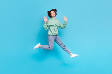 Full length photo of impressed millennial brunette lady jump wave wear pullover jeans sneakers isolated on blue background