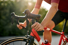 Cropped Unrecognizable Man Dressed In Sportive Cycling Clothes Riding Bicycle On Asphalt Out-of-town Path. Active Sporty People Concept Image. Close-up Photo Of Hands, Copy Space