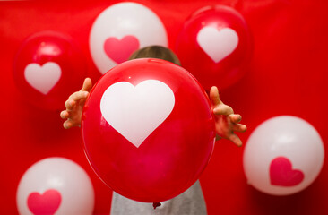 Wall Mural - The boy with heart balloons congratulates with valentine's day, on a red background.