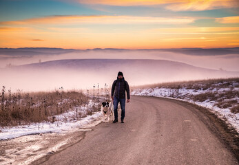 man with his dog in foggy winter landscape at sunset