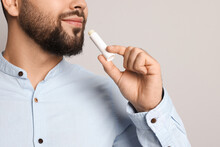 Young Man Applying Lip Balm On Grey Background, Closeup