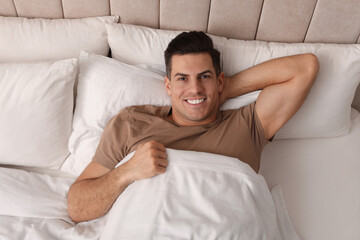 Wall Mural - Happy man lying in bed at home, top view