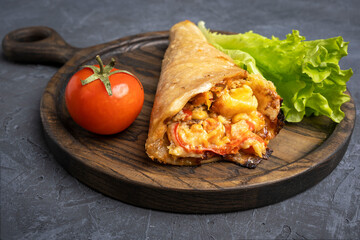 Pizza cone, fresh lettuce leaf and tomato on an oak chopping board.