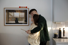 Young Couple Looking At Picture Frame Hanging On Wall