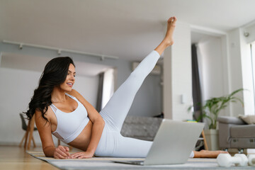 Wall Mural - Young fit woman in sportswear watching online video with fitness exercises on laptop