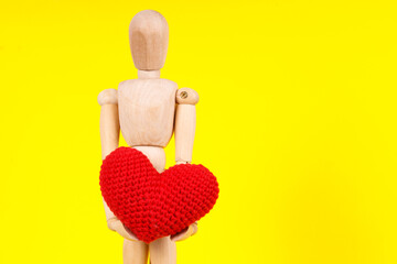 Poster - wooden man with a red heart in his hands on a yellow background