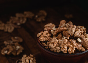 Wall Mural - Walnut kernels close up in a brown ceramic bowl on a dark wooden background.