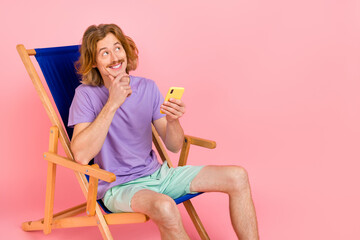 Poster - Portrait of handsome trendy cheery guy sitting in chair using device thinking post 5g isolated over pink pastel color background