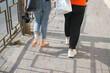 © Sergio - Girlfriend walking barefoot on sidewalk holding high-heeled shoes, back view. Close-up of bare feet ona sunny day, outdoors