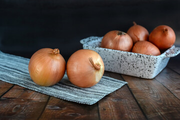 Freshly dug bulbs on a wooden surface against a dark background. Onions after harvesting from the village garden. Bio products for a healthy lifestyle.