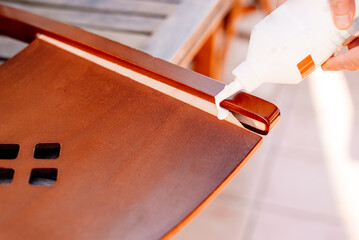 Person applies wood glue to glue loose boards from a broken chair.