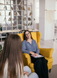a satisfied therapist sits in a chair and talks to a patient at a reception in the room. Home psychotherapy